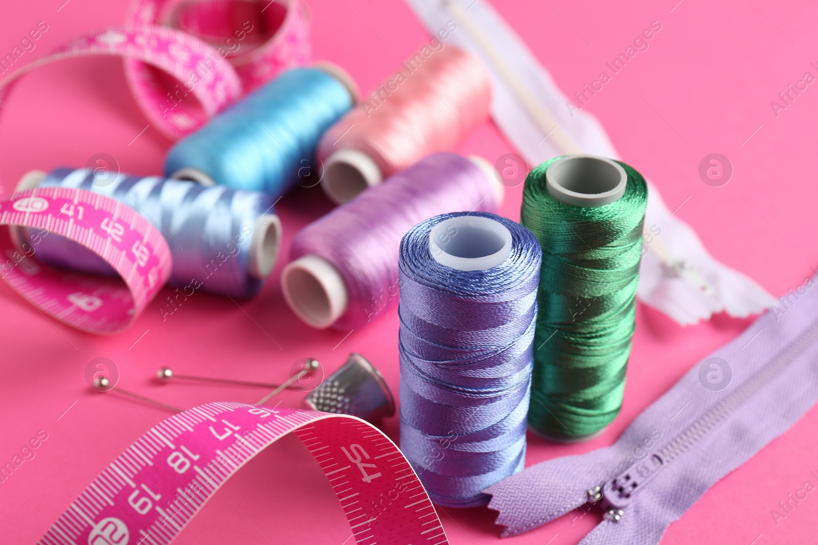 Photo of Different sewing supplies on pink background, closeup