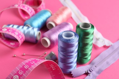 Photo of Different sewing supplies on pink background, closeup