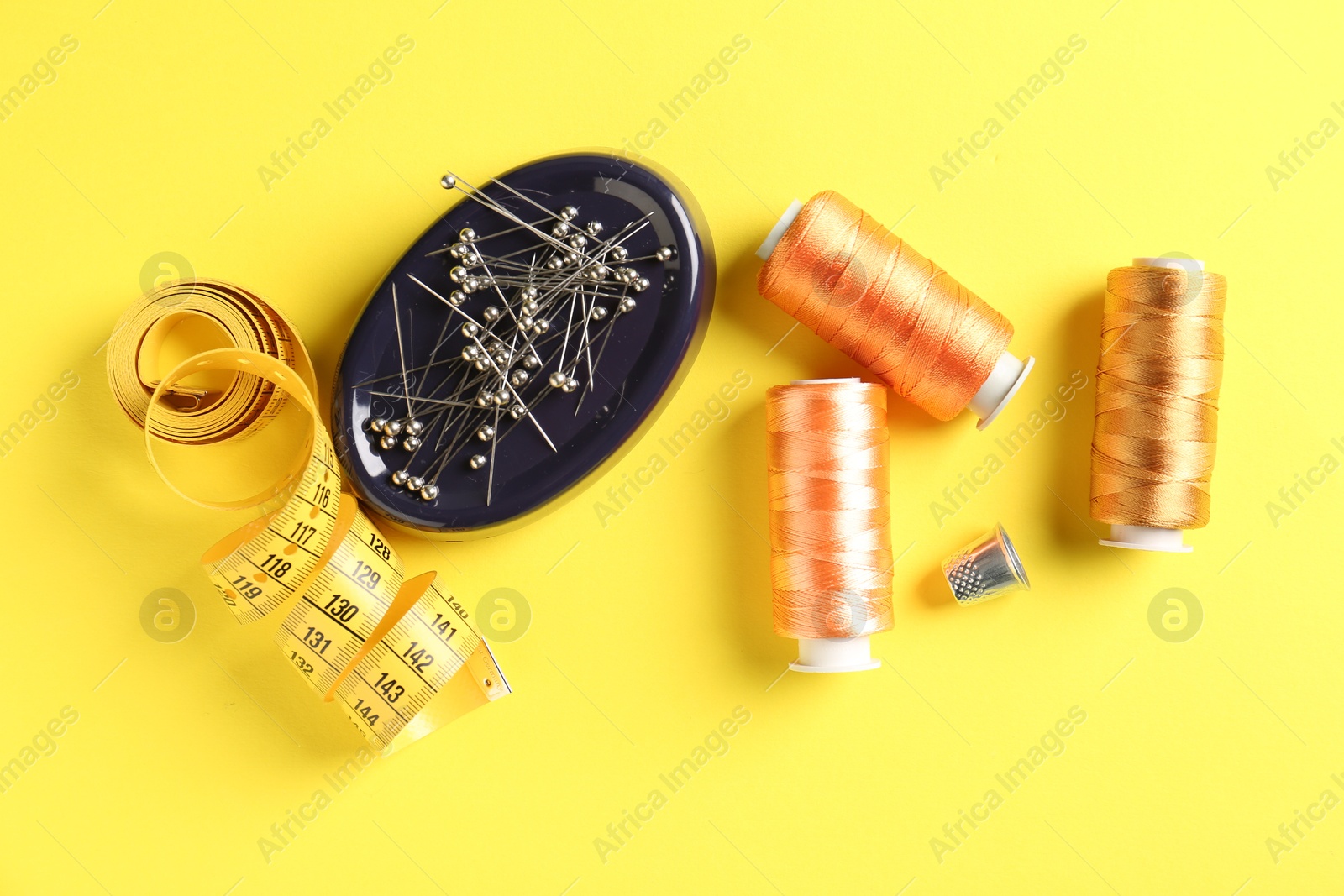 Photo of Different sewing supplies on yellow background, flat lay