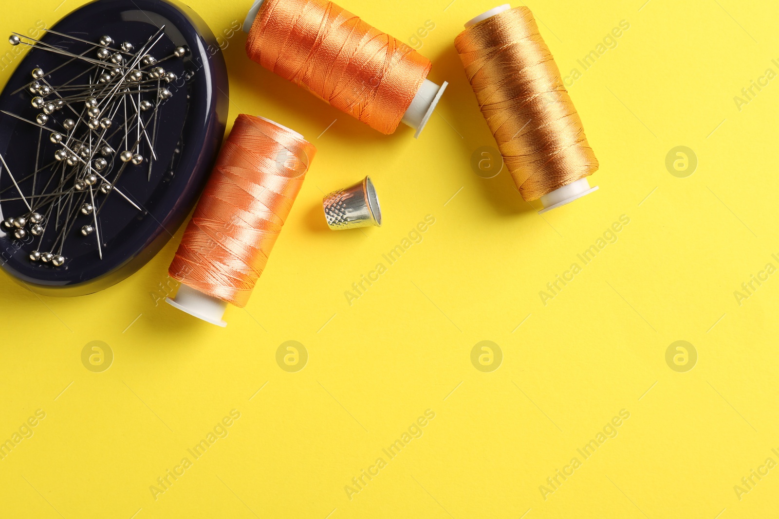 Photo of Different sewing supplies on yellow background, flat lay. Space for text