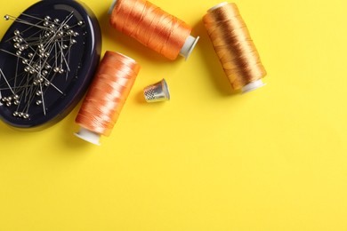 Photo of Different sewing supplies on yellow background, flat lay. Space for text