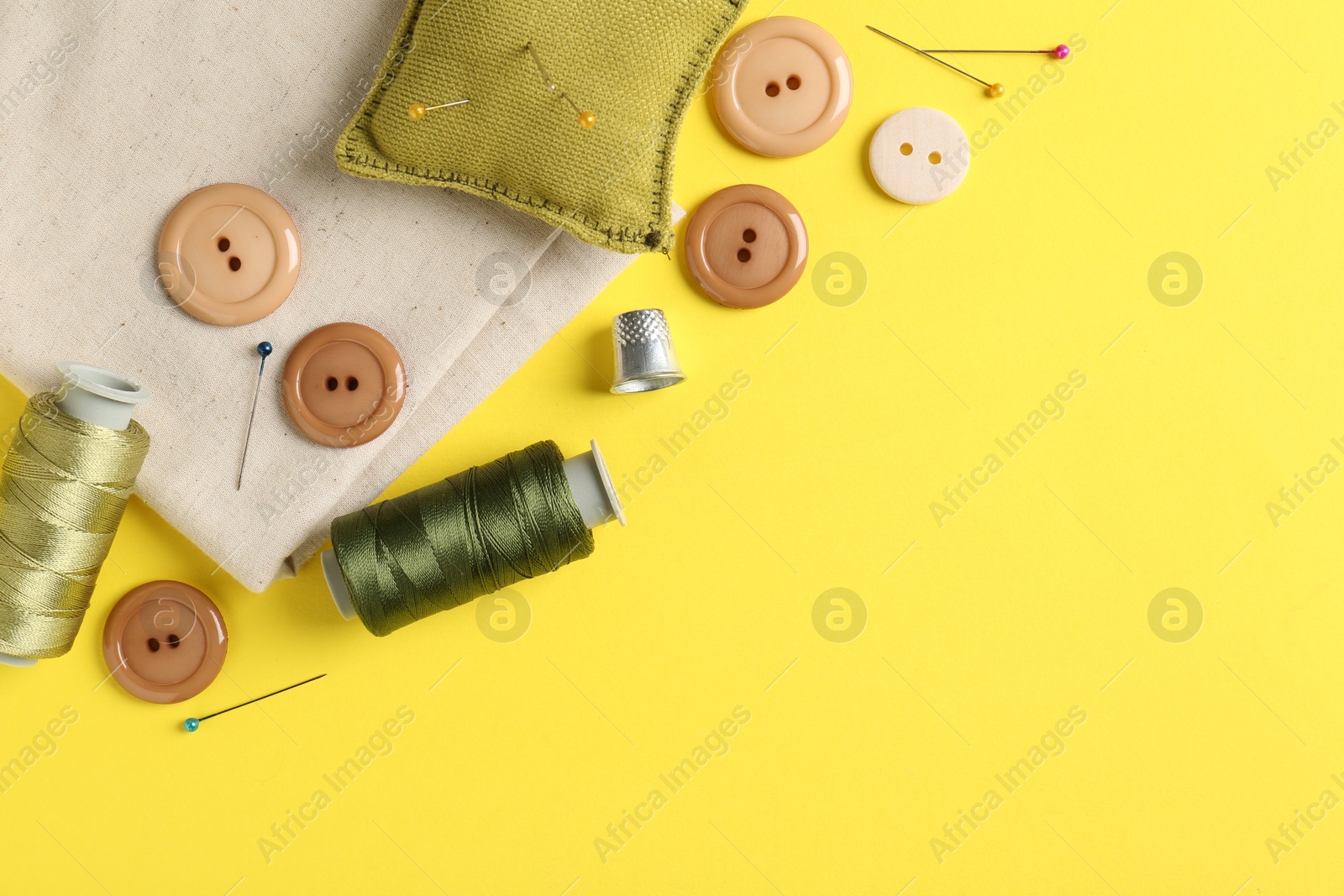 Photo of Different sewing supplies on yellow background, flat lay. Space for text