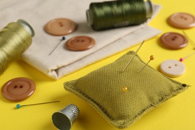 Photo of Different sewing supplies on yellow background, closeup