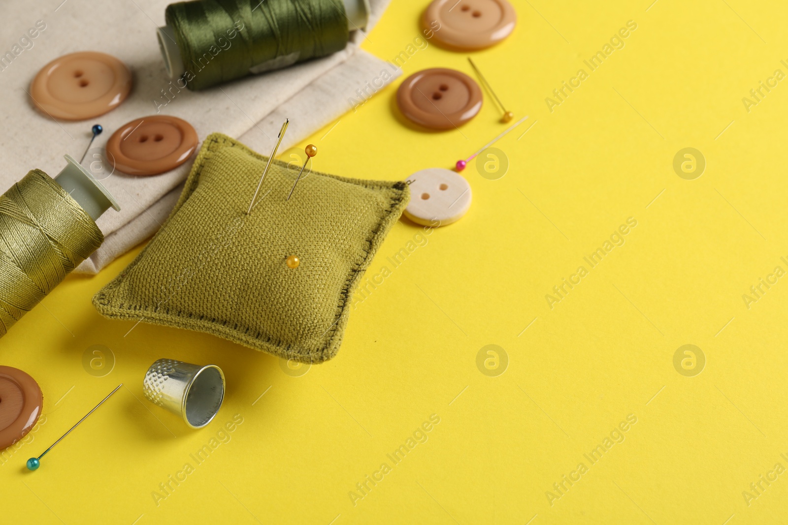 Photo of Different sewing supplies on yellow background, closeup. Space for text