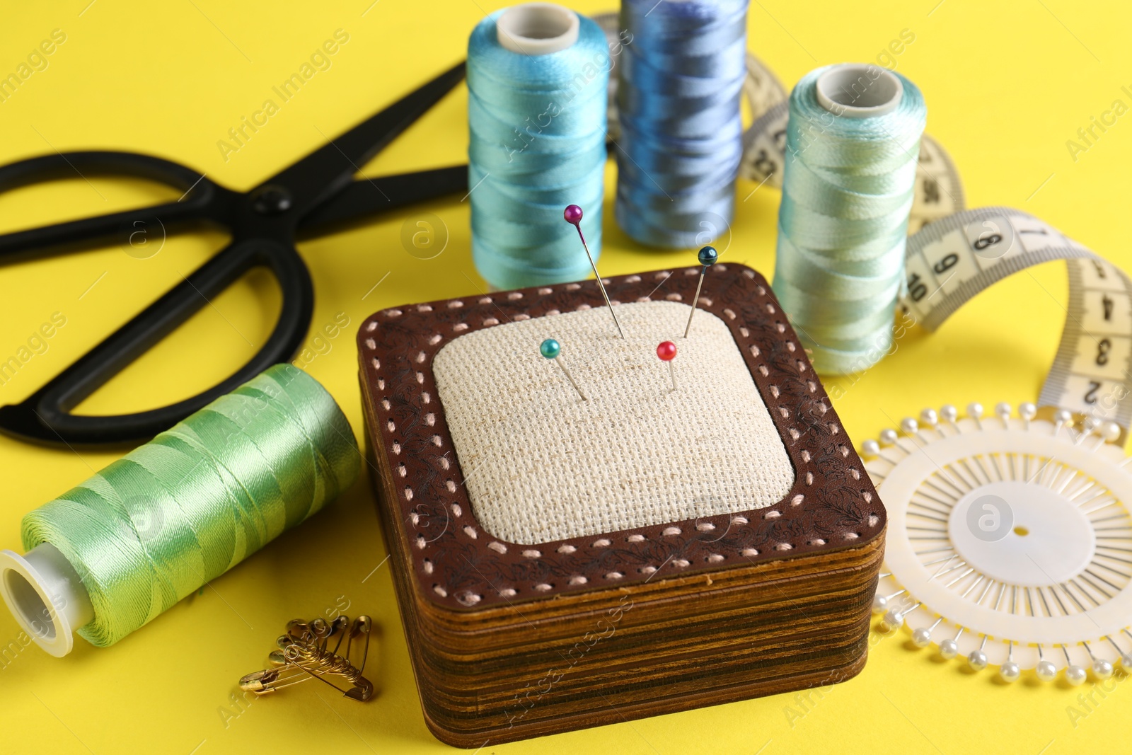 Photo of Different sewing supplies on yellow background, closeup