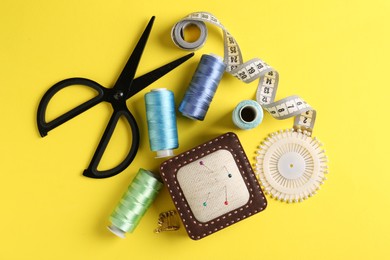 Photo of Different sewing supplies on yellow background, flat lay