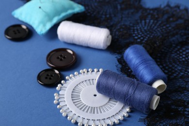 Photo of Different sewing supplies on blue background, closeup