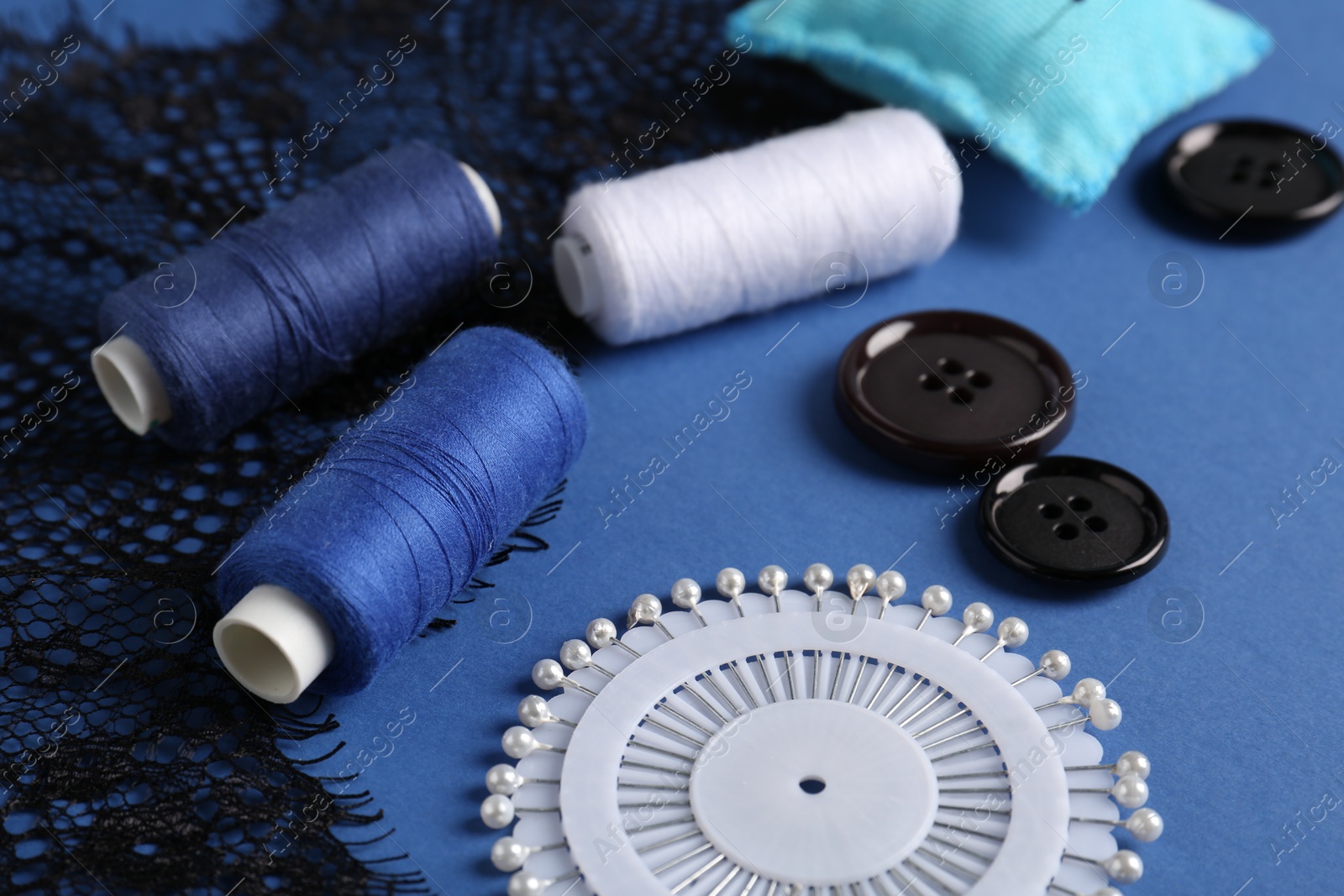 Photo of Different sewing supplies on blue background, closeup