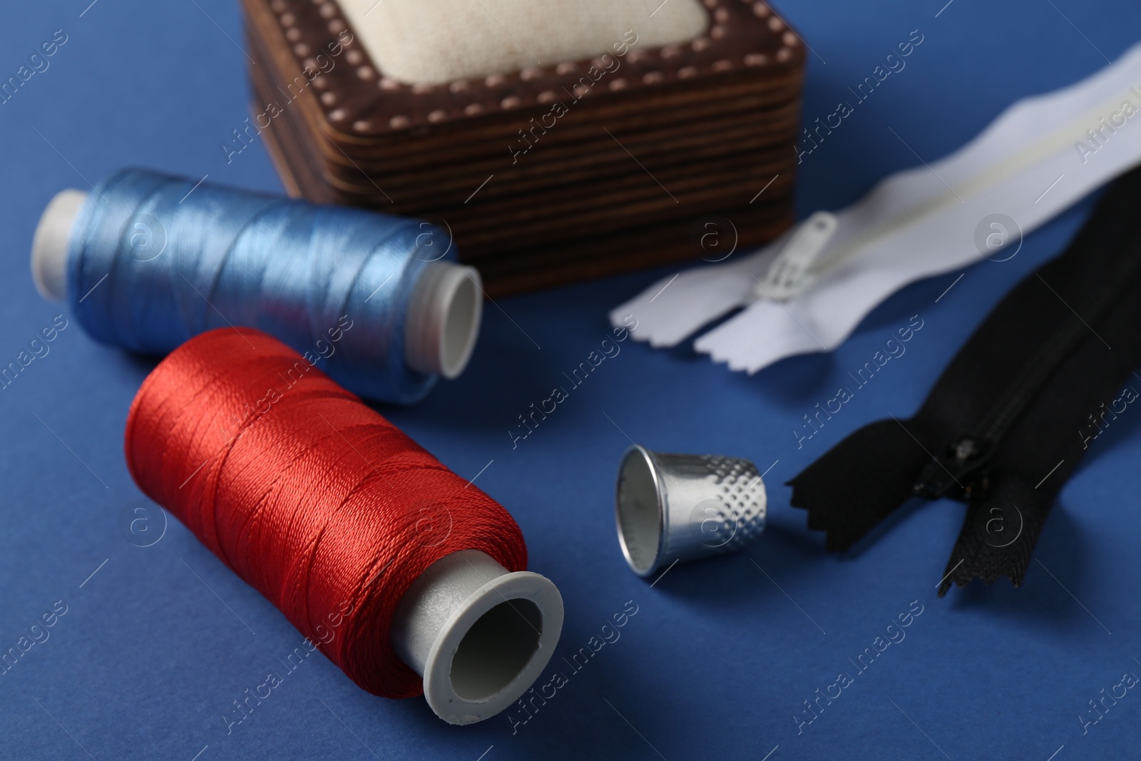 Photo of Different sewing supplies on blue background, closeup