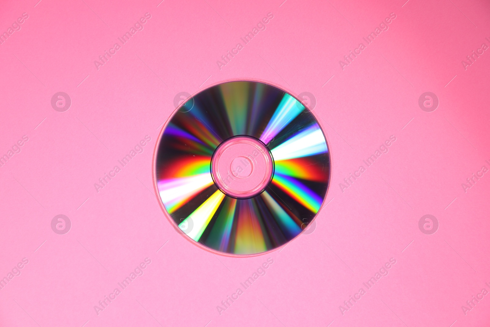 Photo of One shiny compact disc on pink background, top view