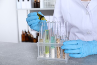 Photo of Laboratory testing. Scientist dripping sample into test tube at grey table indoors, closeup