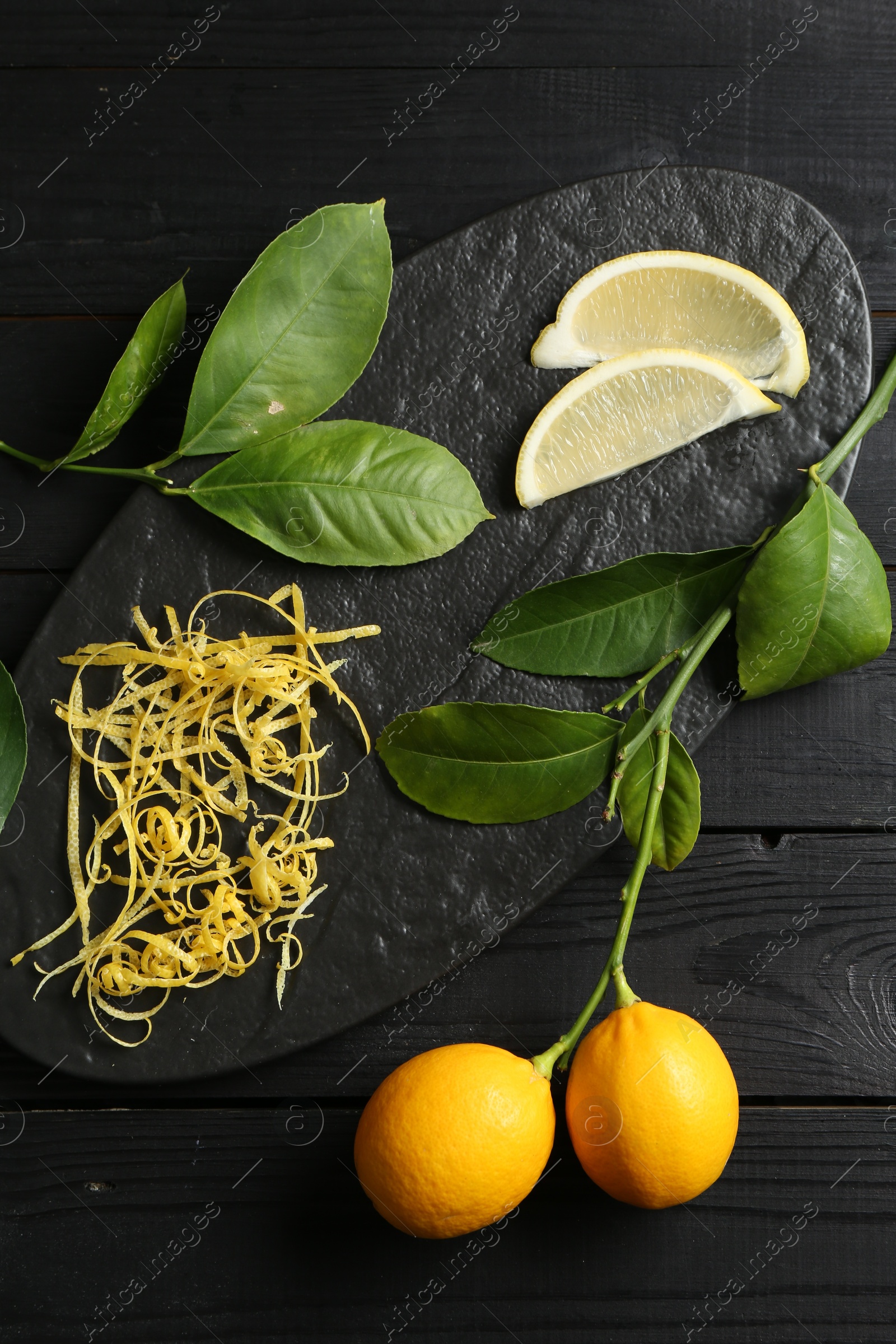 Photo of Lemon zest, fresh fruits, slices and leaves on black wooden table, top view