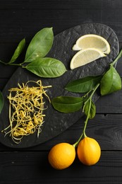 Photo of Lemon zest, fresh fruits, slices and leaves on black wooden table, top view