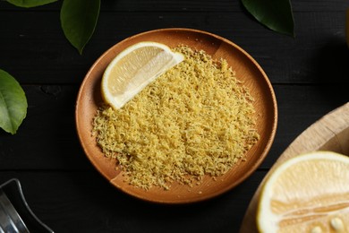 Photo of Lemon zest with fresh fruit slice on black wooden table, closeup