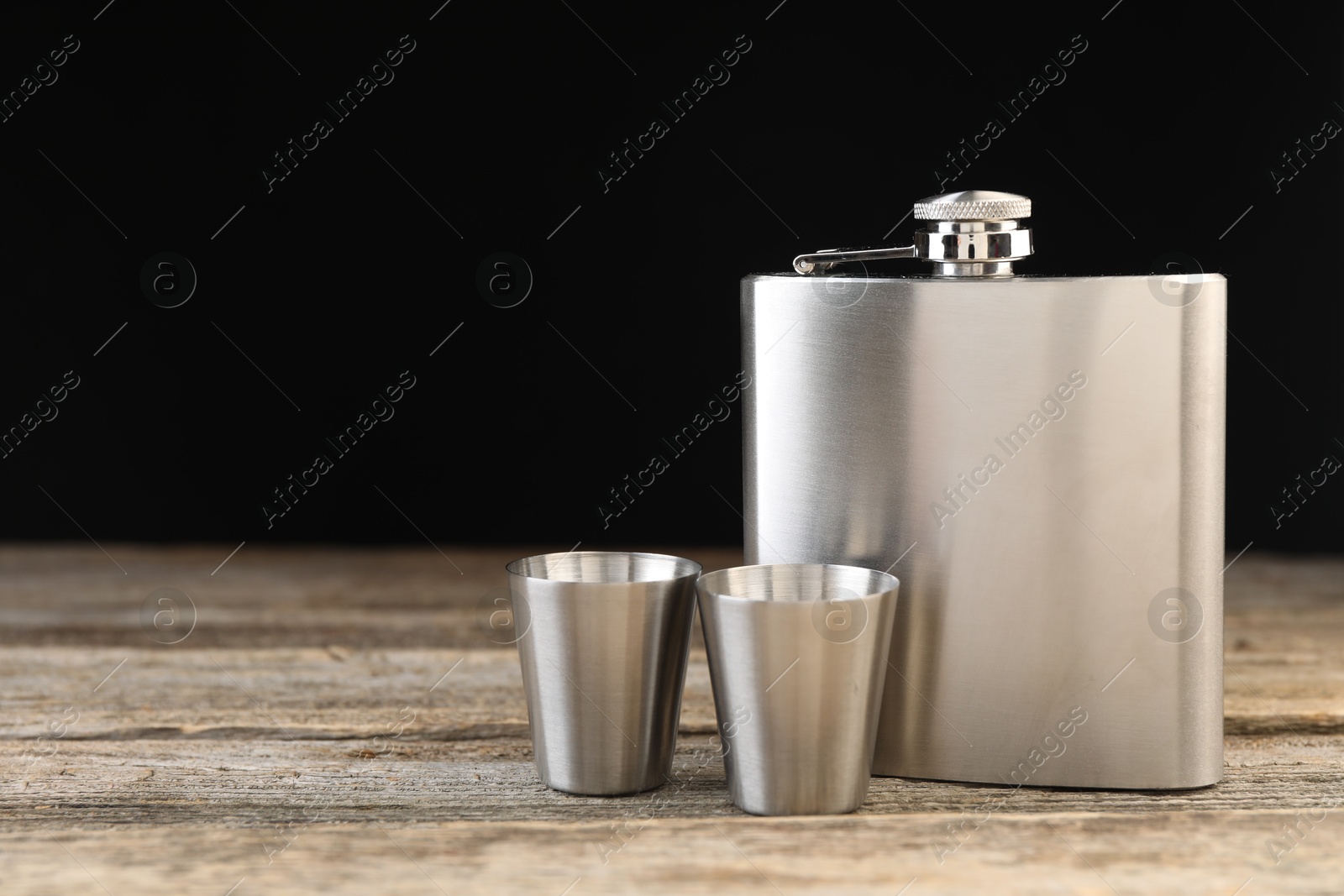 Photo of Hip flask and cups on wooden table, space for text