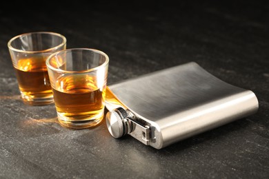 Photo of Hip flask and shot glasses of whiskey on black table, closeup