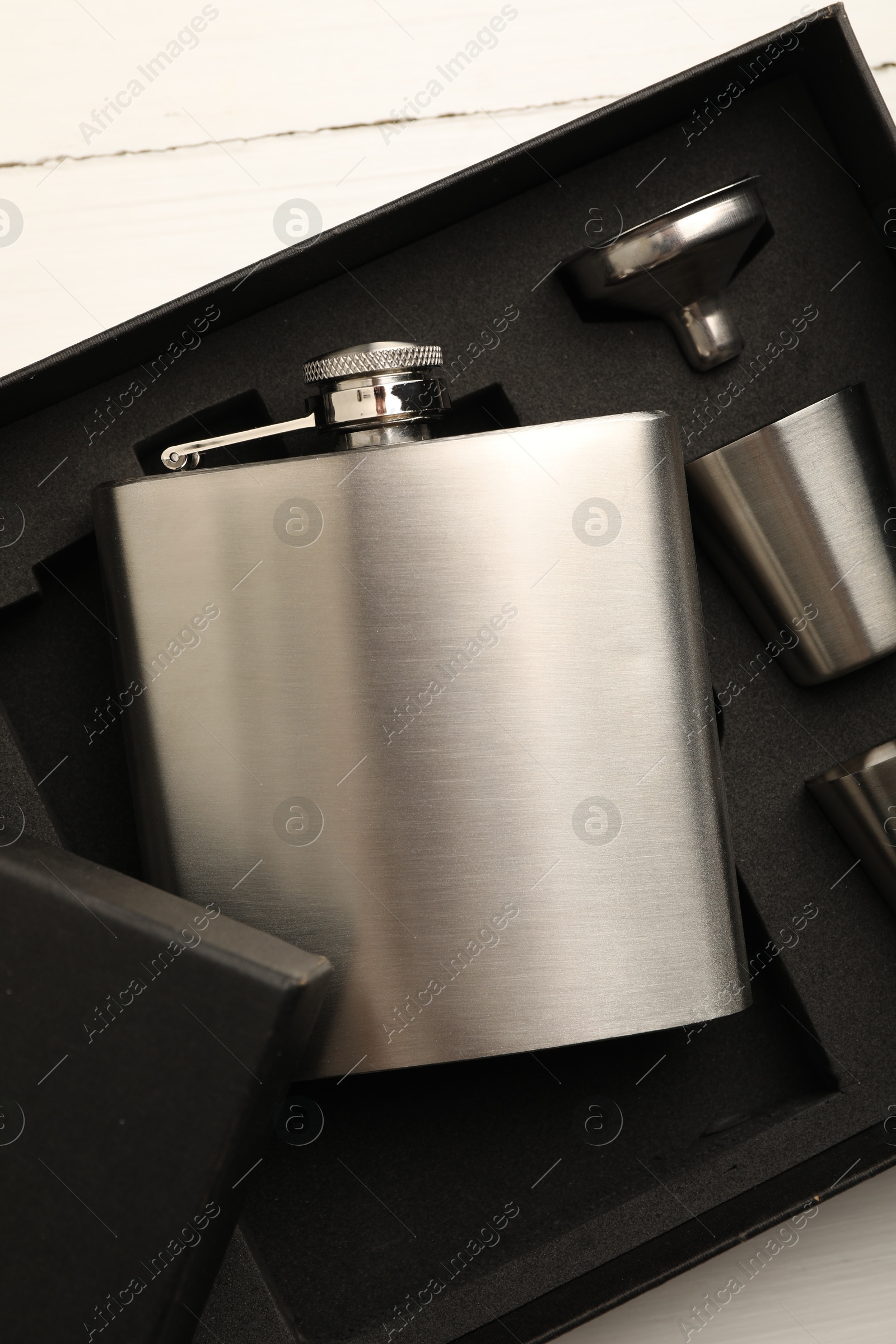 Photo of Hip flask, cups and funnel in package on white wooden table, top view