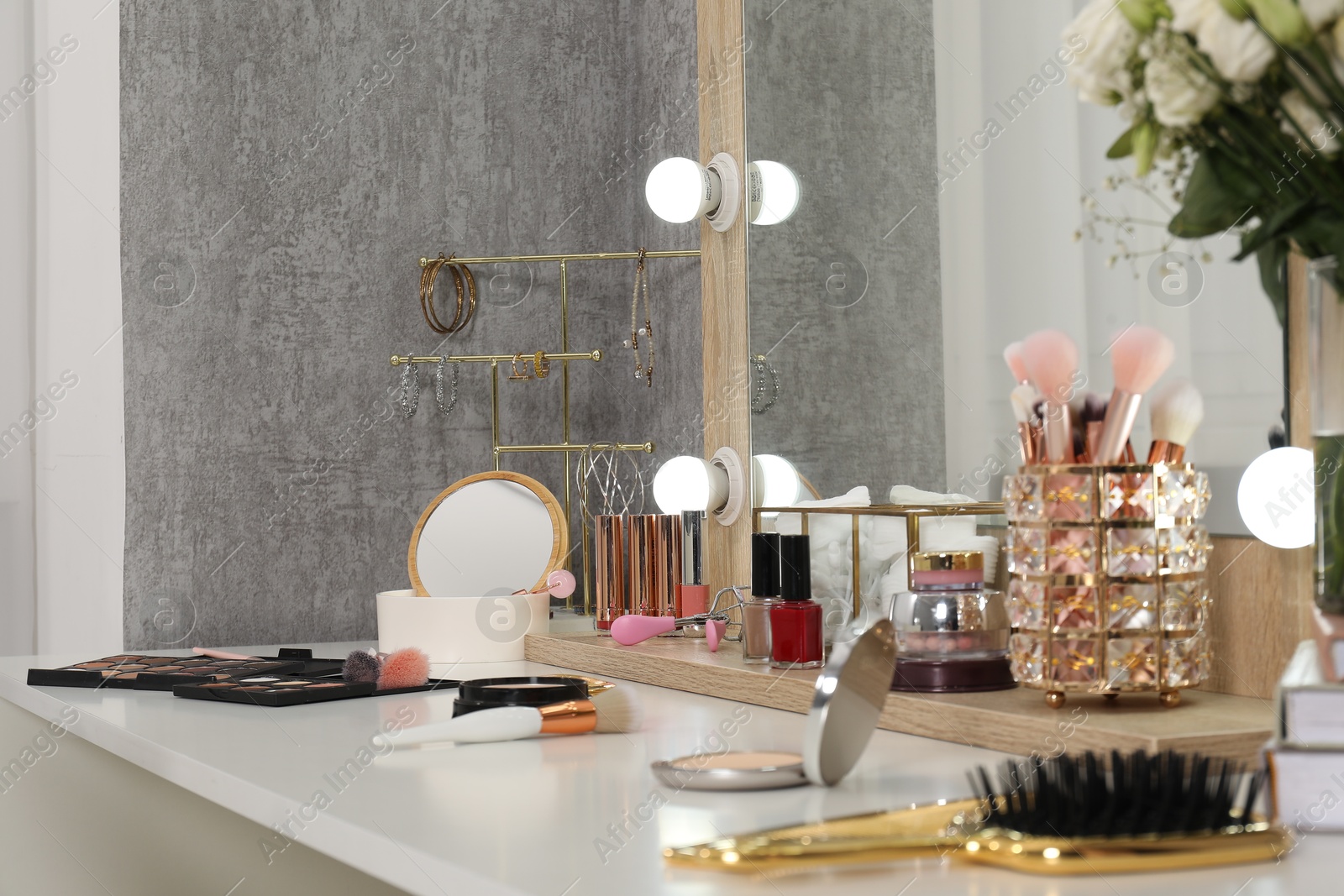 Photo of Makeup room. Mirror, different beauty products and jewelry on dressing table indoors