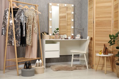 Photo of Makeup room. Mirror, dressing table, different beauty products, shoes, clothing rack and chair indoors