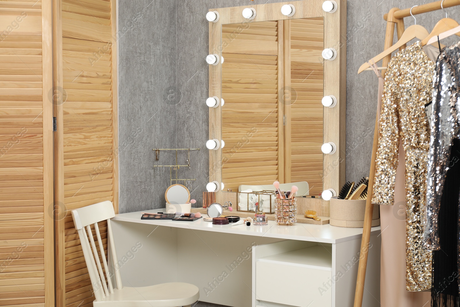 Photo of Makeup room. Mirror, dressing table, different beauty products, clothing rack and chair indoors