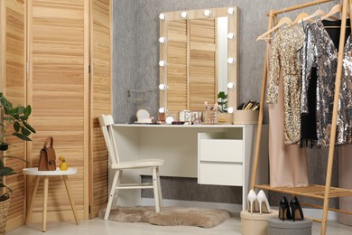 Photo of Makeup room. Mirror, dressing table, different beauty products, shoes, clothing rack and chair indoors