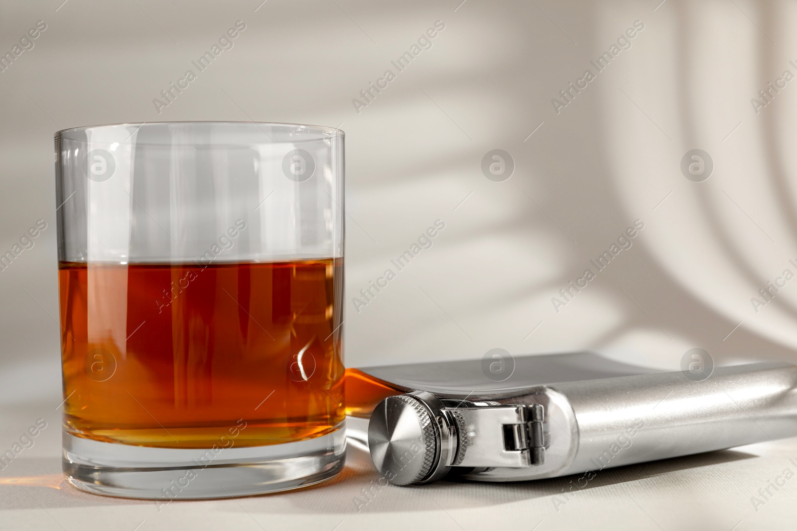 Photo of Hip flask and glass of whiskey on light table, closeup