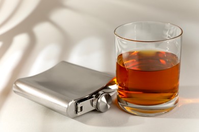 Photo of Hip flask and glass of whiskey on light table, closeup