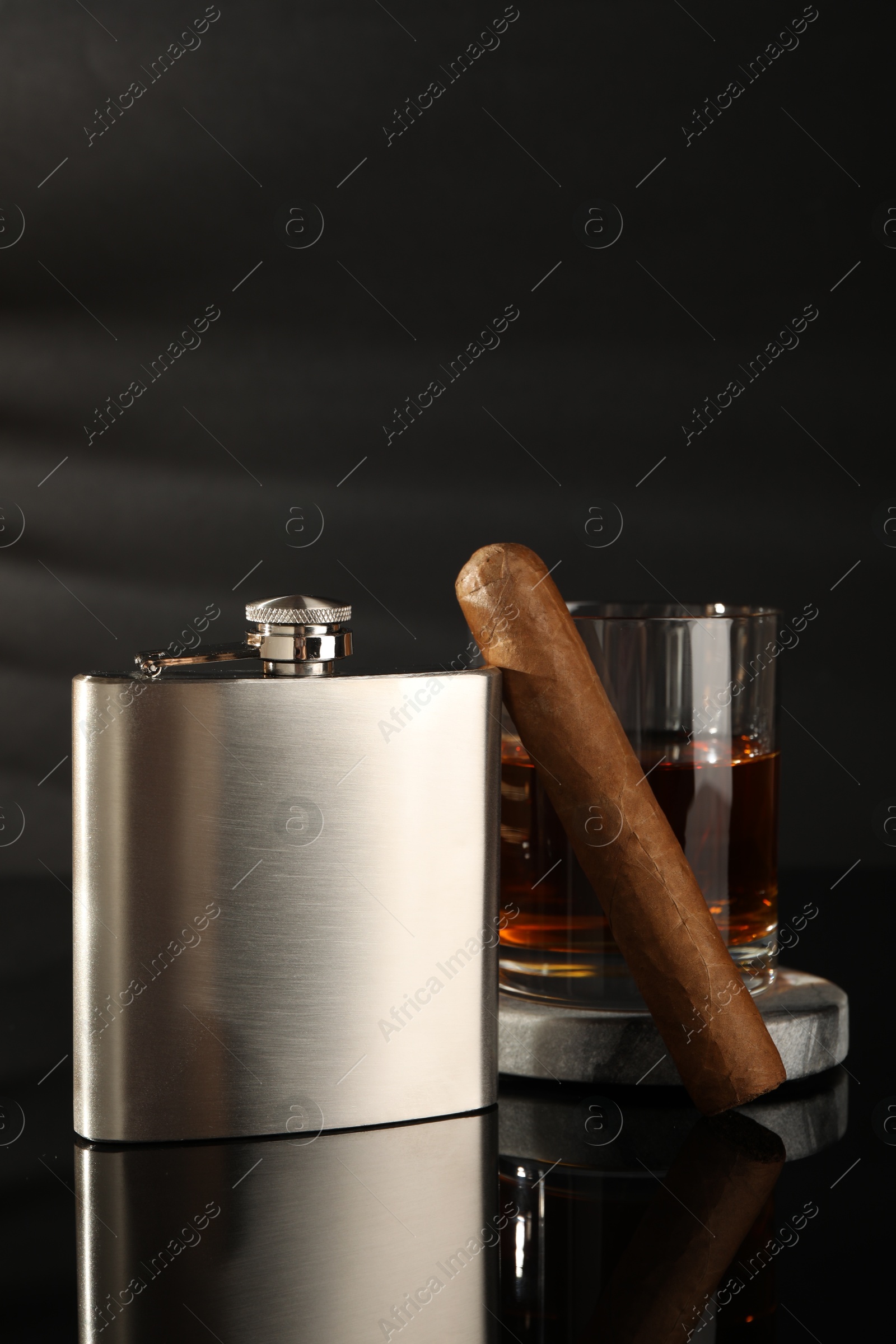 Photo of Hip flask, glass of whiskey and cigar on black mirror surface