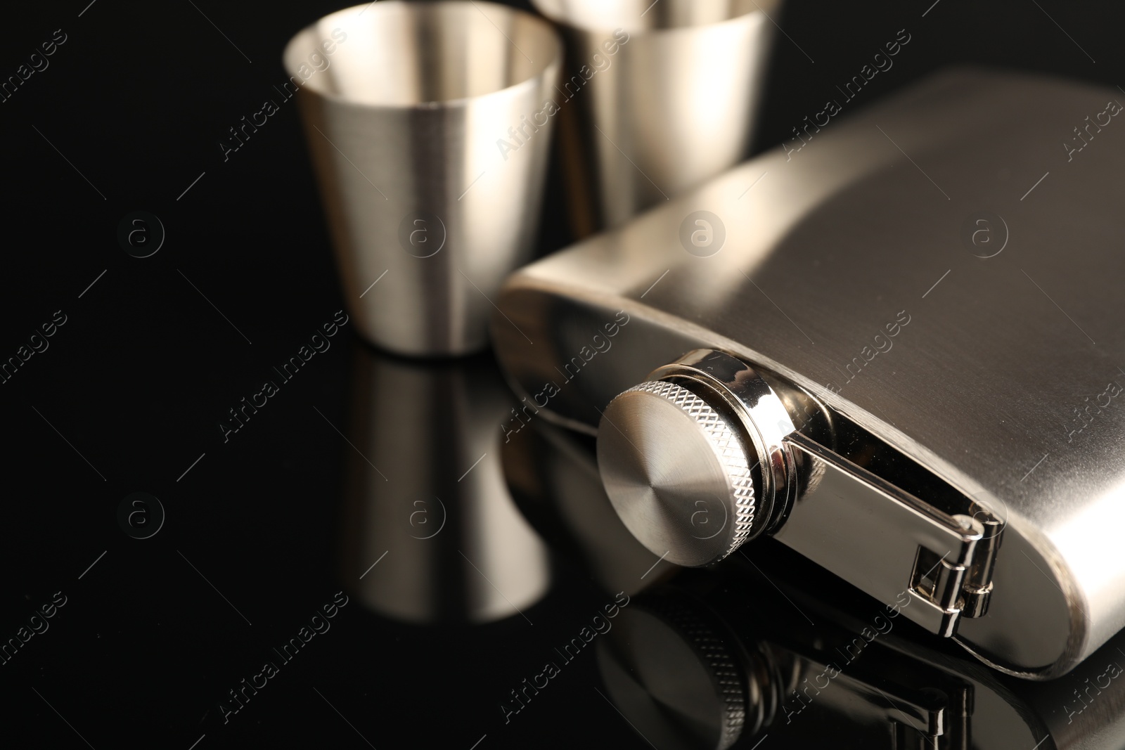 Photo of Hip flask and cups on black mirror surface, closeup. Space for text