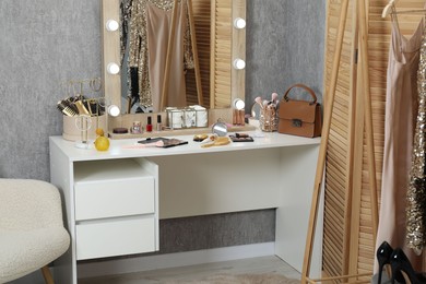 Photo of Makeup room. Mirror, dressing table, different beauty products and clothing rack indoors