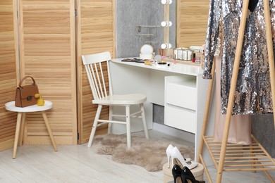 Photo of Makeup room. Mirror, dressing table, different beauty products, clothing rack and chair indoors