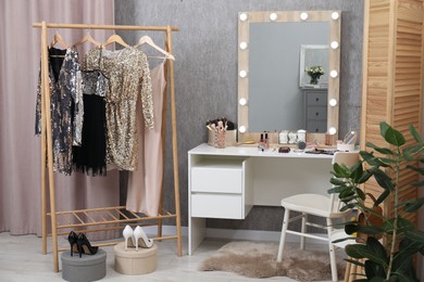 Photo of Makeup room. Mirror, dressing table, different beauty products, clothing rack and chair indoors