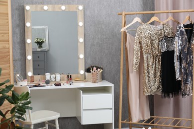 Photo of Makeup room. Mirror, dressing table, different beauty products, clothing rack and chair indoors