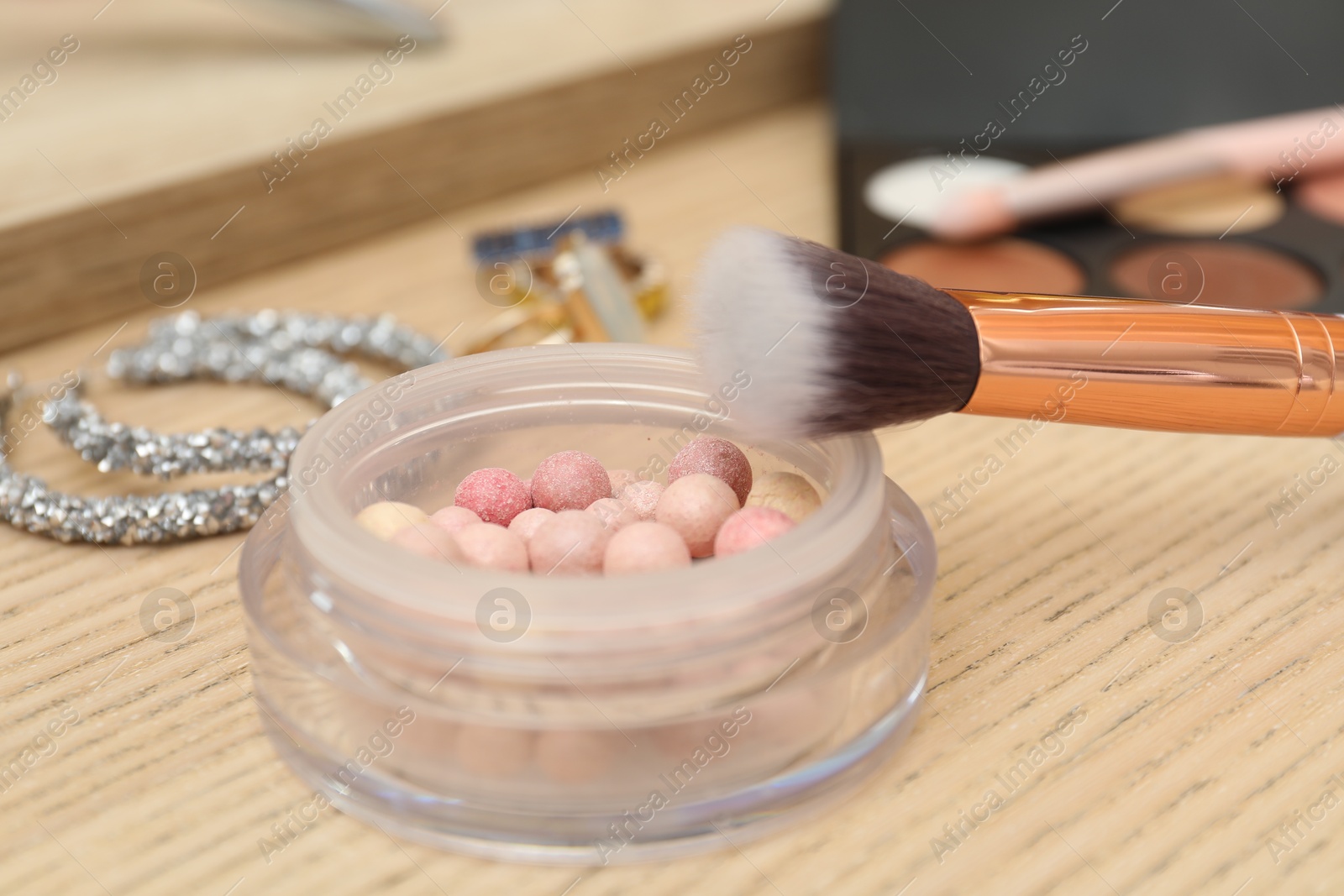 Photo of Makeup room. Blush, brush and jewelry on wooden table, closeup