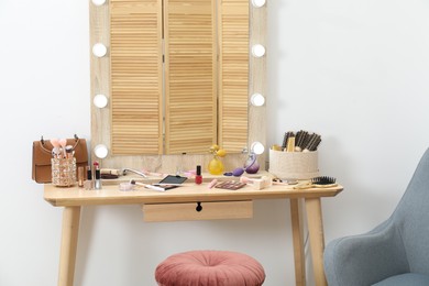 Photo of Makeup room. Mirror, wooden dressing table, different beauty products, stool and armchair indoors