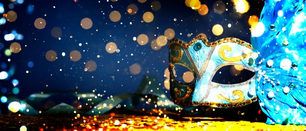 Image of Beautiful carnival mask on dark blue background with glitter, bokeh effect. Banner design with space for text