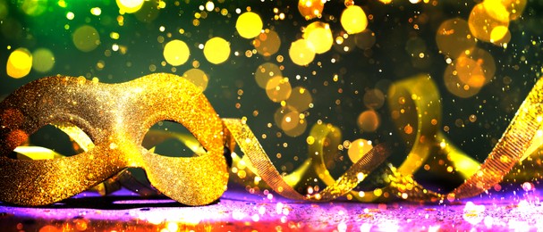 Image of Beautiful carnival mask and streamers on black background with glitter, bokeh effect. Banner design with space for text