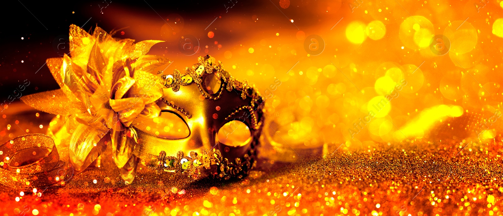 Image of Beautiful carnival mask on golden background with glitter, bokeh effect. Banner design with space for text