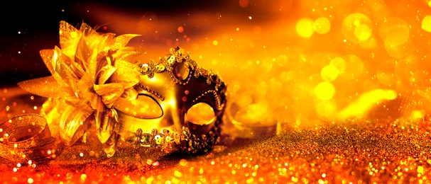 Image of Beautiful carnival mask on golden background with glitter, bokeh effect. Banner design with space for text