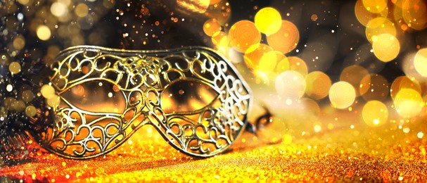 Image of Beautiful carnival mask on black background with golden glitter, bokeh effect. Banner design with space for text