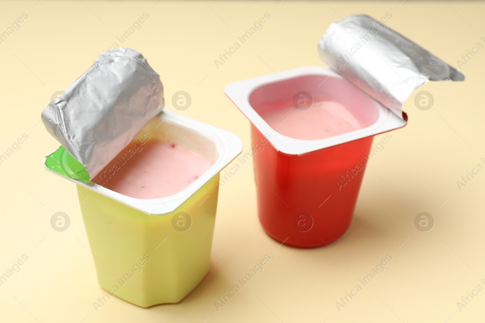 Photo of Delicious yogurts in plastic cups on beige background, closeup