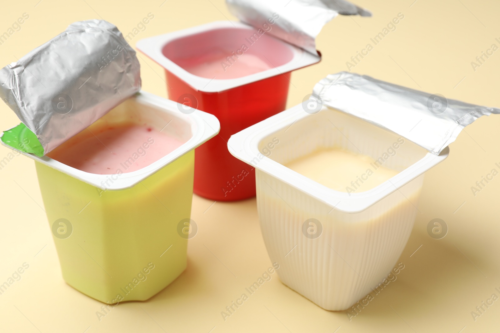 Photo of Delicious yogurts in plastic cups on beige background, closeup