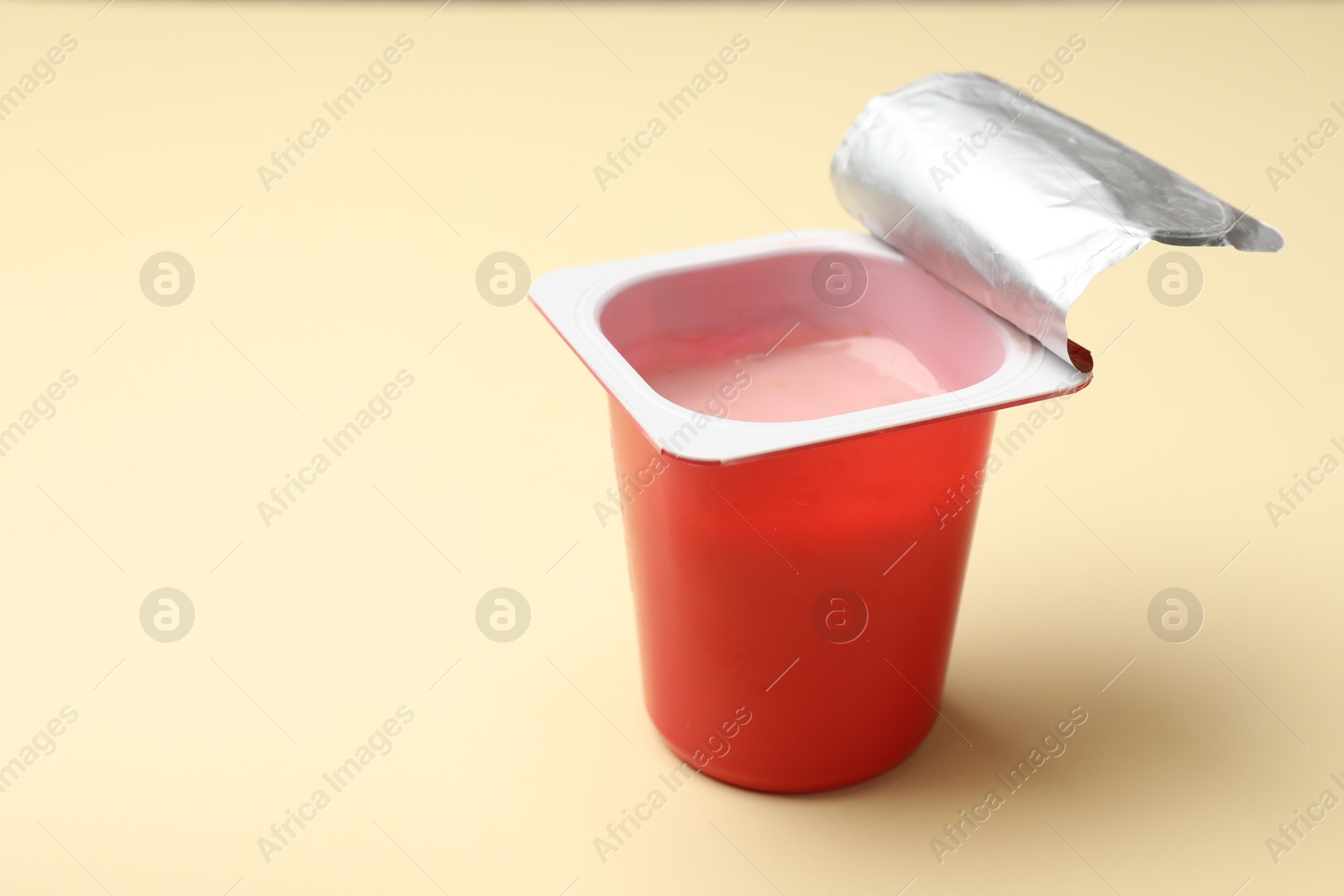 Photo of Delicious yogurt in plastic cup on beige background, closeup. Space for text