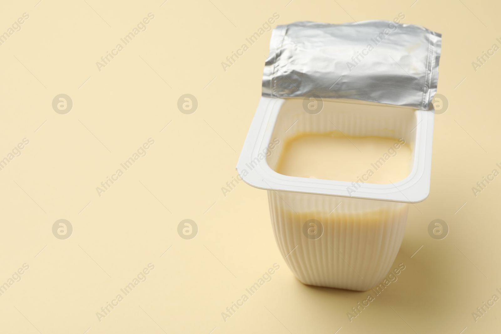 Photo of Delicious yogurt in plastic cup on beige background, closeup. Space for text