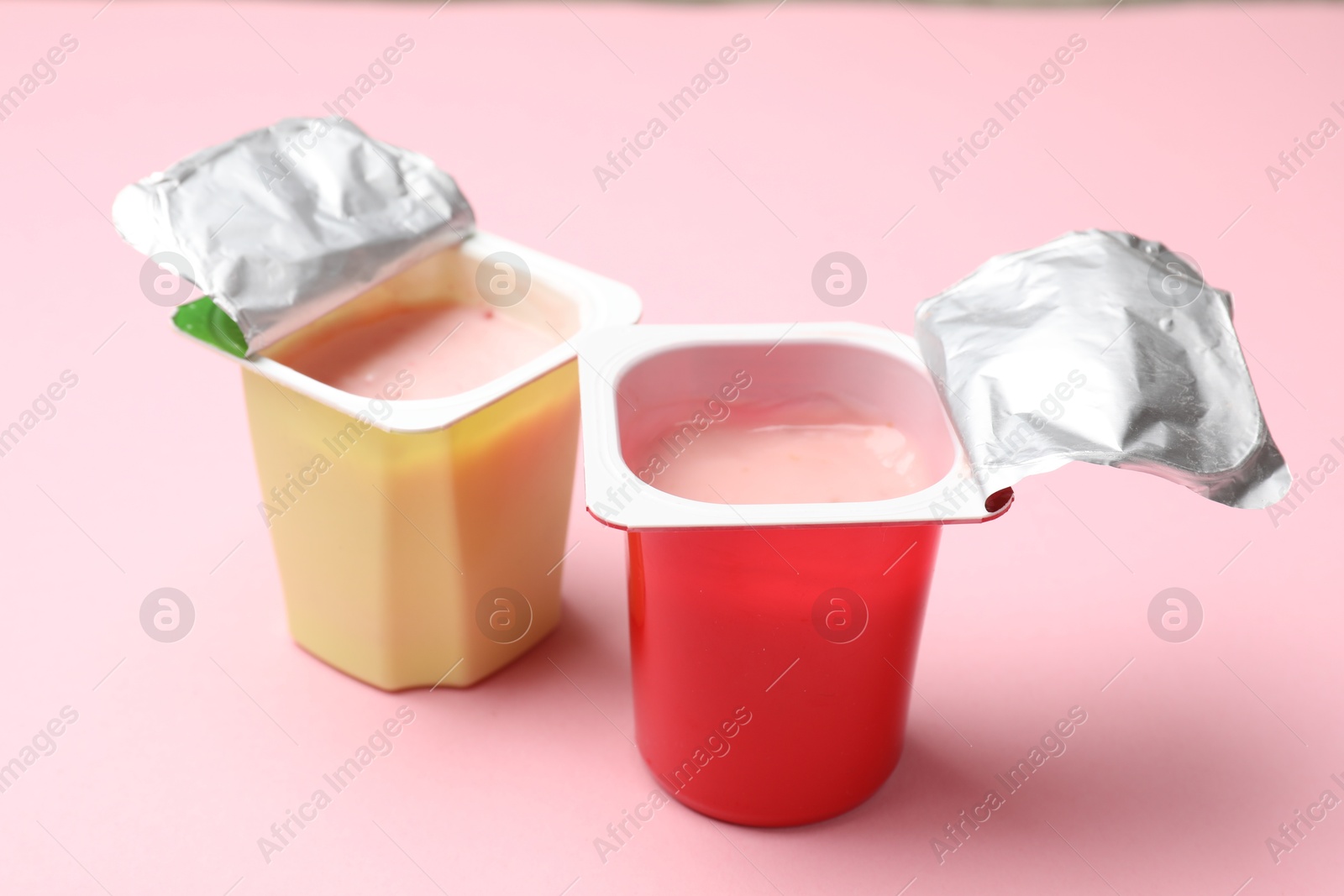 Photo of Delicious yogurts in plastic cups on light pink background, closeup