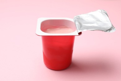 Photo of Delicious yogurt in plastic cup on light pink background, closeup