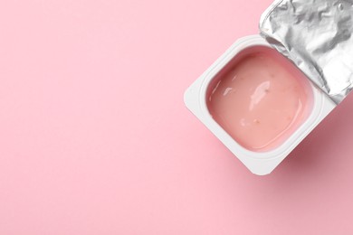 Photo of Delicious yogurt in plastic cup on light pink background, top view. Space for text