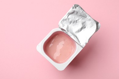 Photo of Delicious yogurt in plastic cup on light pink background, top view