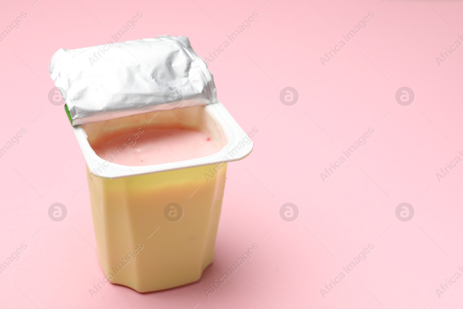 Photo of Delicious yogurt in plastic cup on light pink background, closeup. Space for text