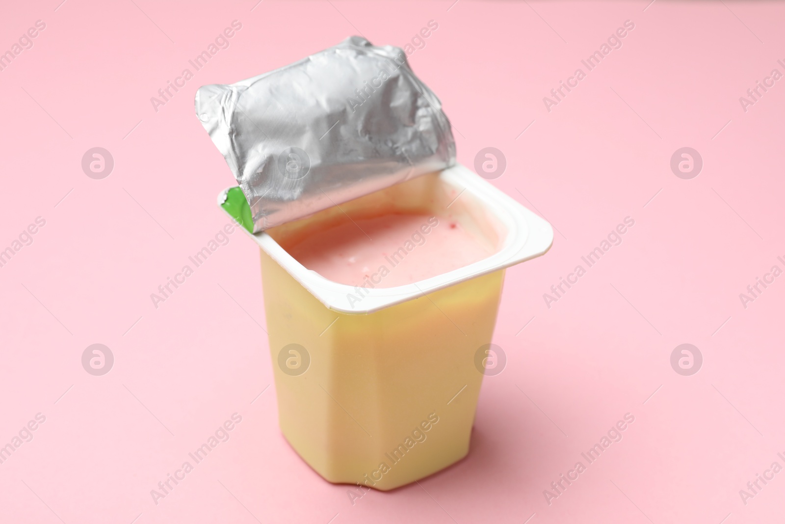 Photo of Delicious yogurt in plastic cup on light pink background, closeup